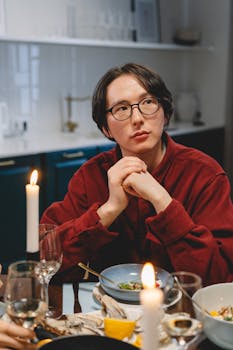 Young man in glasses at a cozy candlelit dinner table with food and drinks.