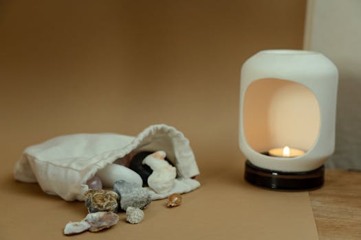 A cozy still life featuring a lit candle in a white ceramic holder next to scattered crystals and seashells.