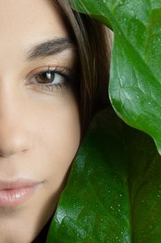 Close-up shot of a woman's face surrounded by vibrant green leaves, highlighting natural beauty.