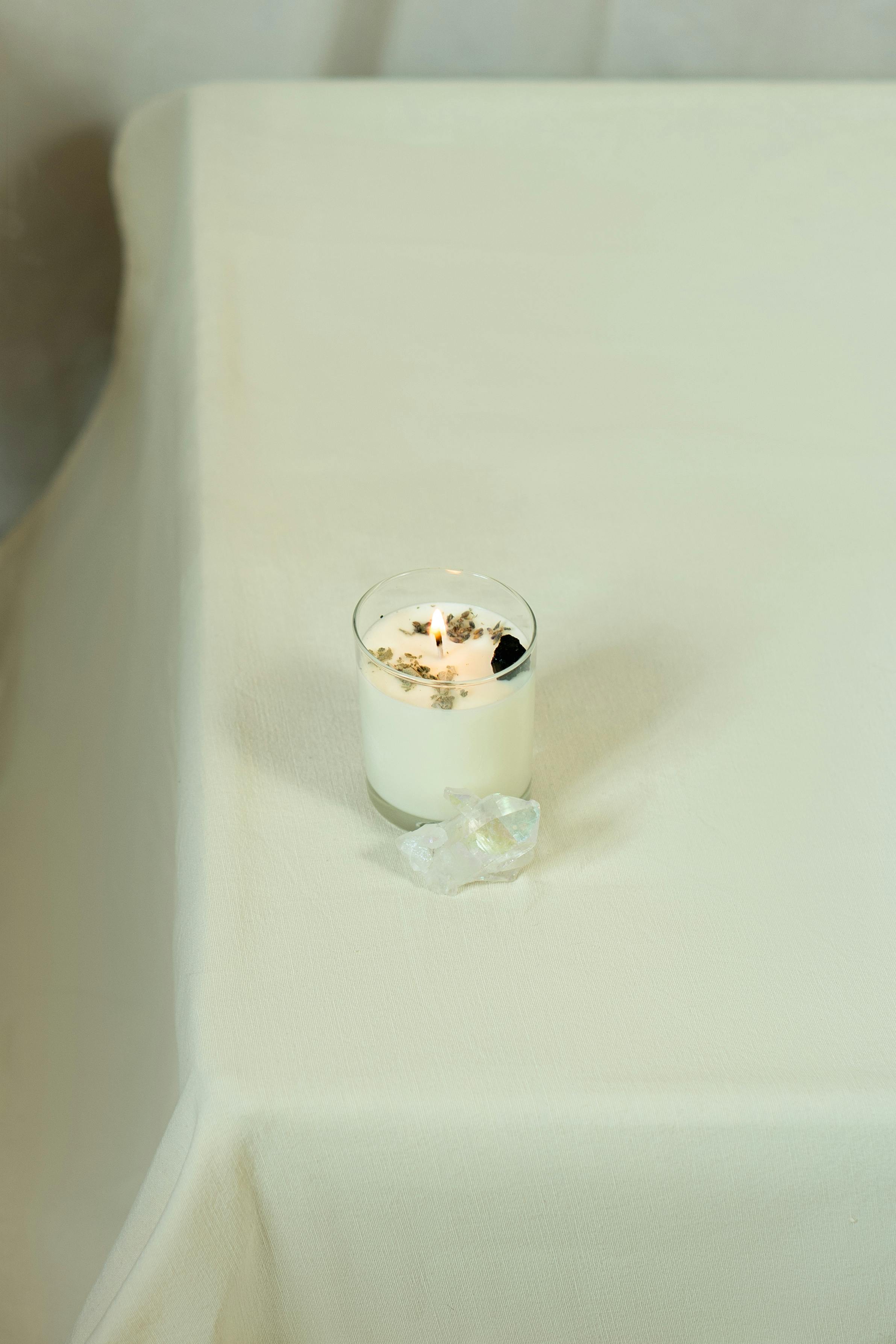 A serene minimalist setup featuring a lit candle alongside a crystal on a neutral-toned table.