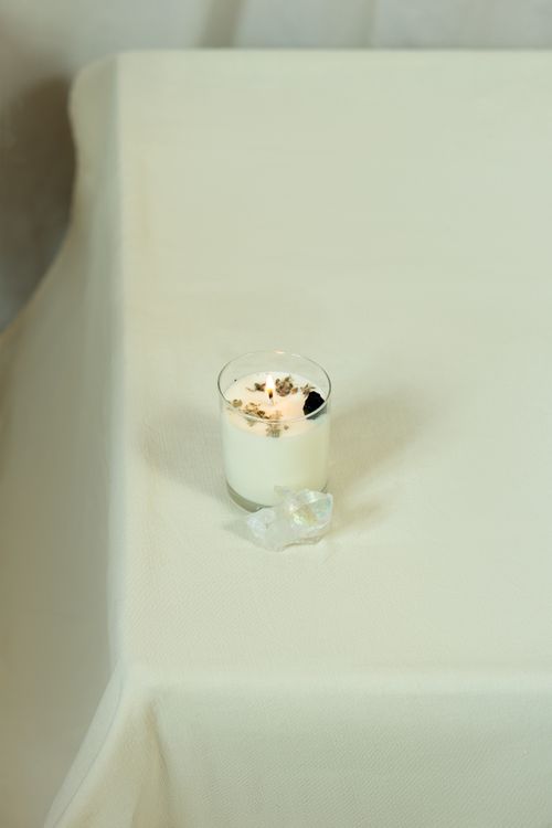Free A serene minimalist setup featuring a lit candle alongside a crystal on a neutral-toned table. Stock Photo