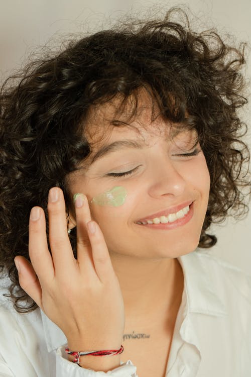 Photo of a Woman Applying Green Cream on Her Face