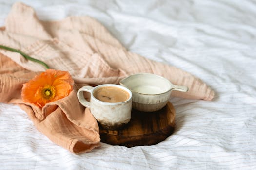 Serene morning setup with coffee, milk jug, and orange poppy on fabric.