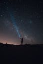 在令人惊叹的星空下，一个人拿着手电筒的剪影，营造出迷人的夜空