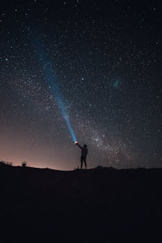 在令人惊叹的星空下，一个人拿着手电筒的剪影，营造出迷人的夜空