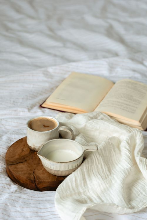 Free A serene setup on a bed featuring an open book, coffee, and milk on a wooden board. Stock Photo