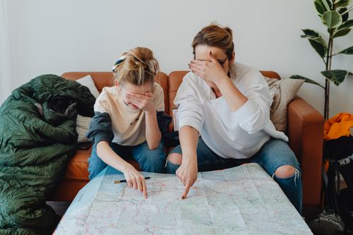Free Mother and daughter covering eyes while pointing at map on couch, planning a trip. Stock Photo