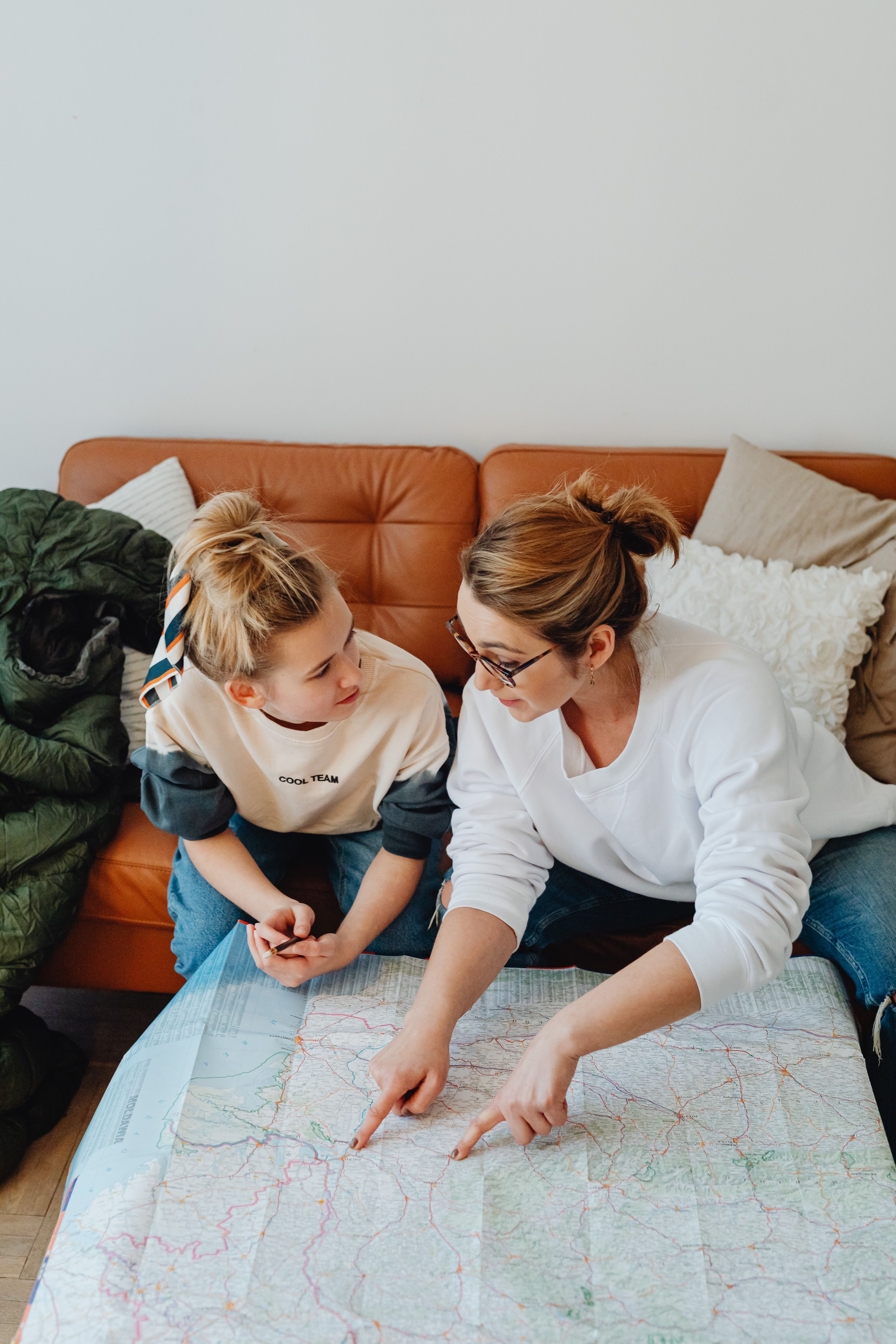 A mother and daughter sitting on a sofa planning travel with a map, sharing a meaningful conversation.