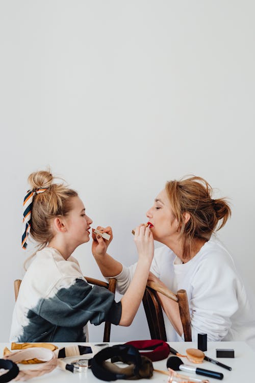 Photo of a Mother and Daughter Applying Lipstick on Each Other