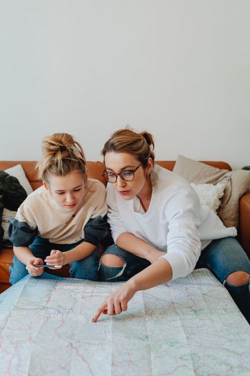 Free Mother and daughter planning a trip with map on the couch, casual setting. Stock Photo