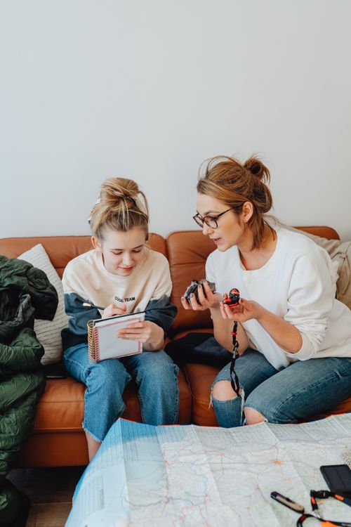 Free A mother and daughter planning a trip with a map and notebook in a cozy living room. Stock Photo