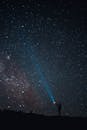 在广阔的星空下，一个人用手电筒照射宇宙，捕捉到一种孤独和神秘的感觉
