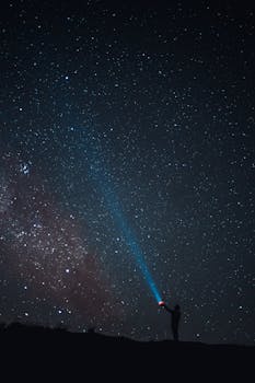 在广阔的星空下，一个人用手电筒照射宇宙，捕捉到一种孤独和神秘的感觉