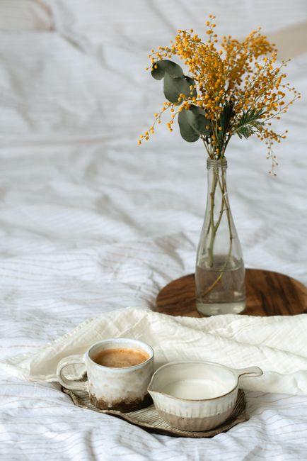 A warm morning scene with coffee, milk, and a vase of yellow flowers on a white blanket.