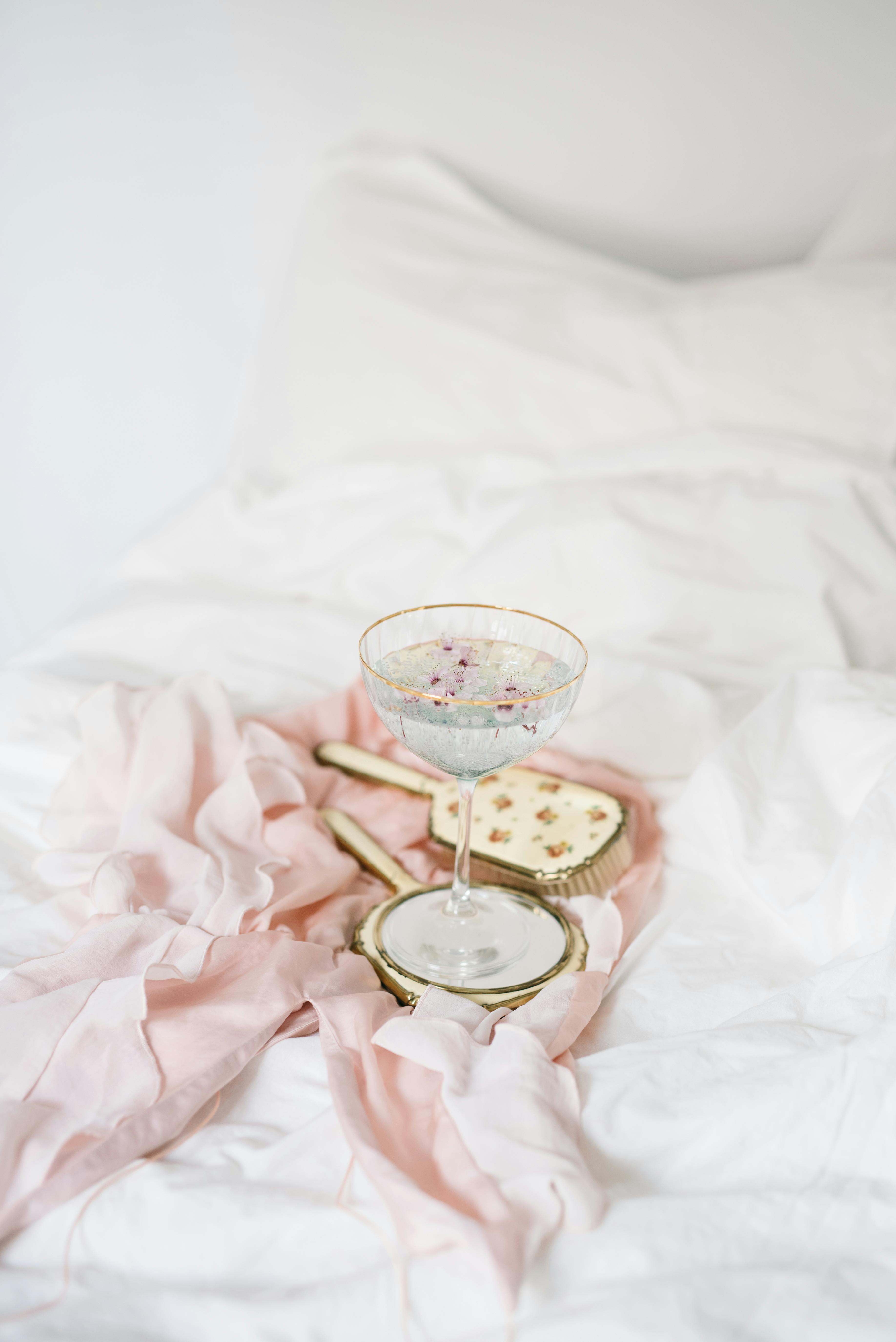 Vintage hand mirror and goblet on soft pink fabric over cozy white bedding, creating an elegant and serene atmosphere.