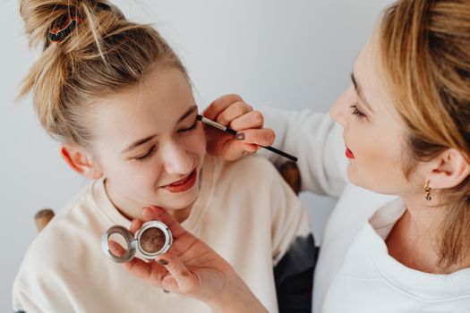 A mother and daughter enjoying a bonding moment while applying makeup together indoors.
