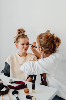 A mother bonding with her daughter by applying makeup in a cozy indoor setting.