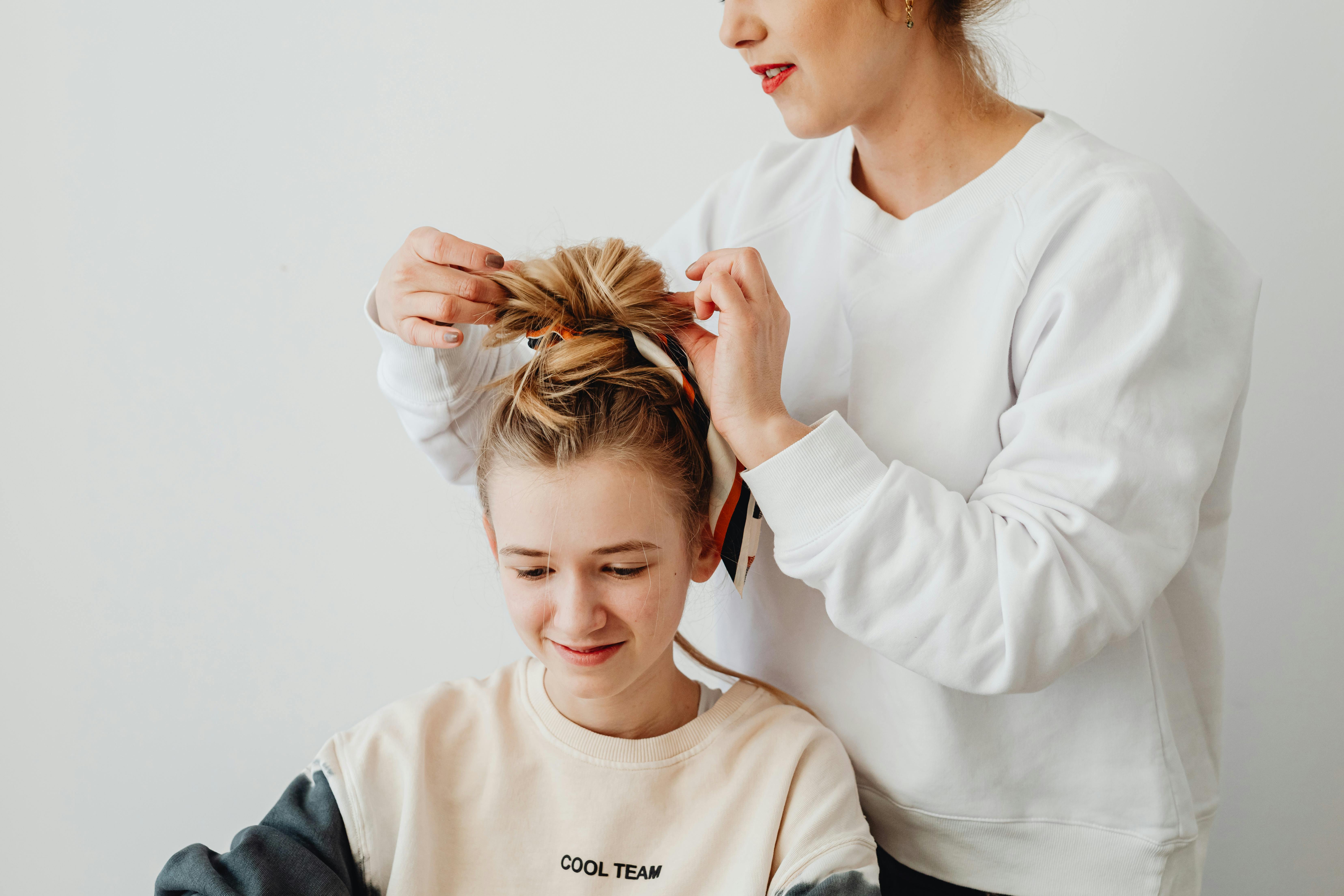 A joyful moment of a mother styling her daughter's hair with care inside a bright room.