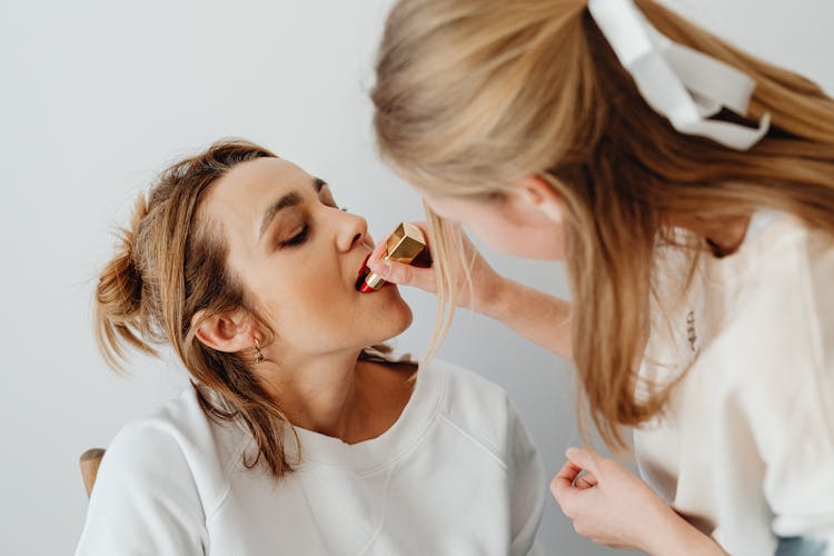 A Woman Putting Lipstick On Another Woman