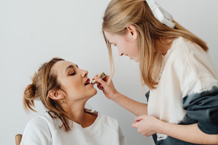 A Girl Applying Lipstick To A Woman