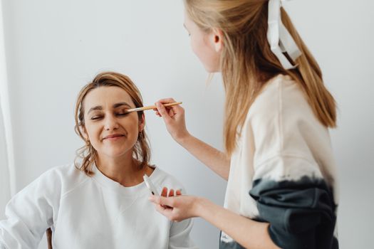 Woman applying makeup on another woman in a cozy indoor setting.