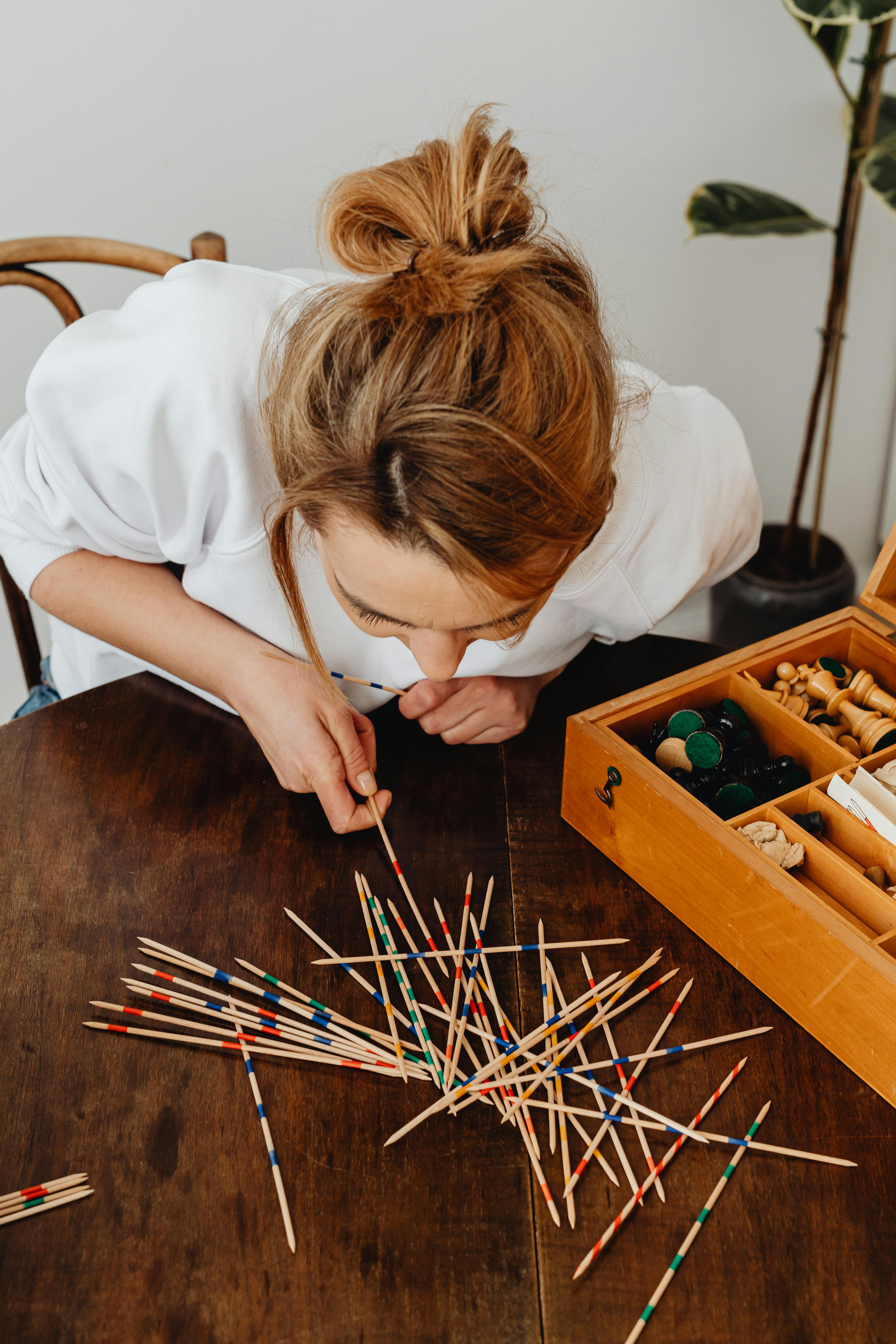 A woman focuses on picking up sticks in a traditional game setup indoors.