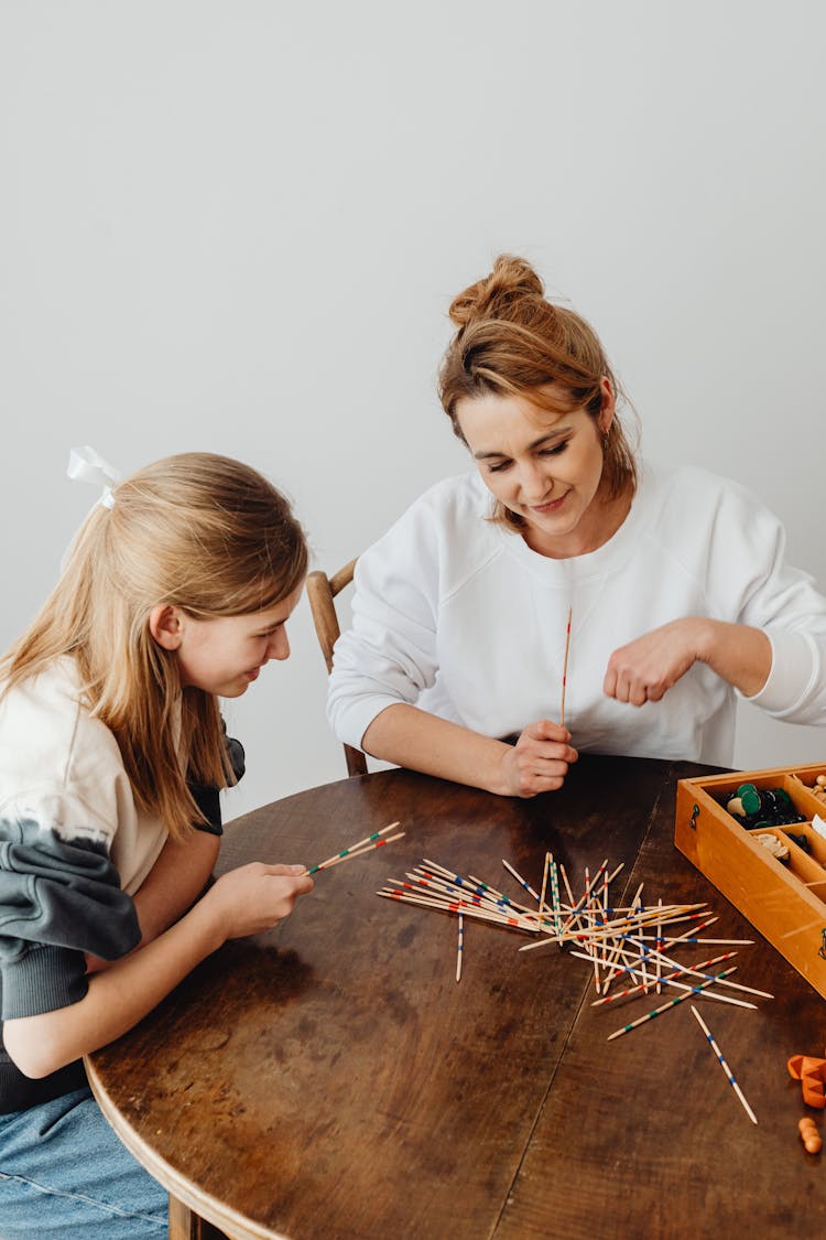 Women Sitting Near The Wooden Table While Holding Sticks