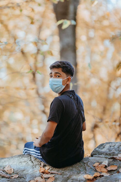 Free Man Wearing a Surgical Mask Sitting on a Rock  Stock Photo