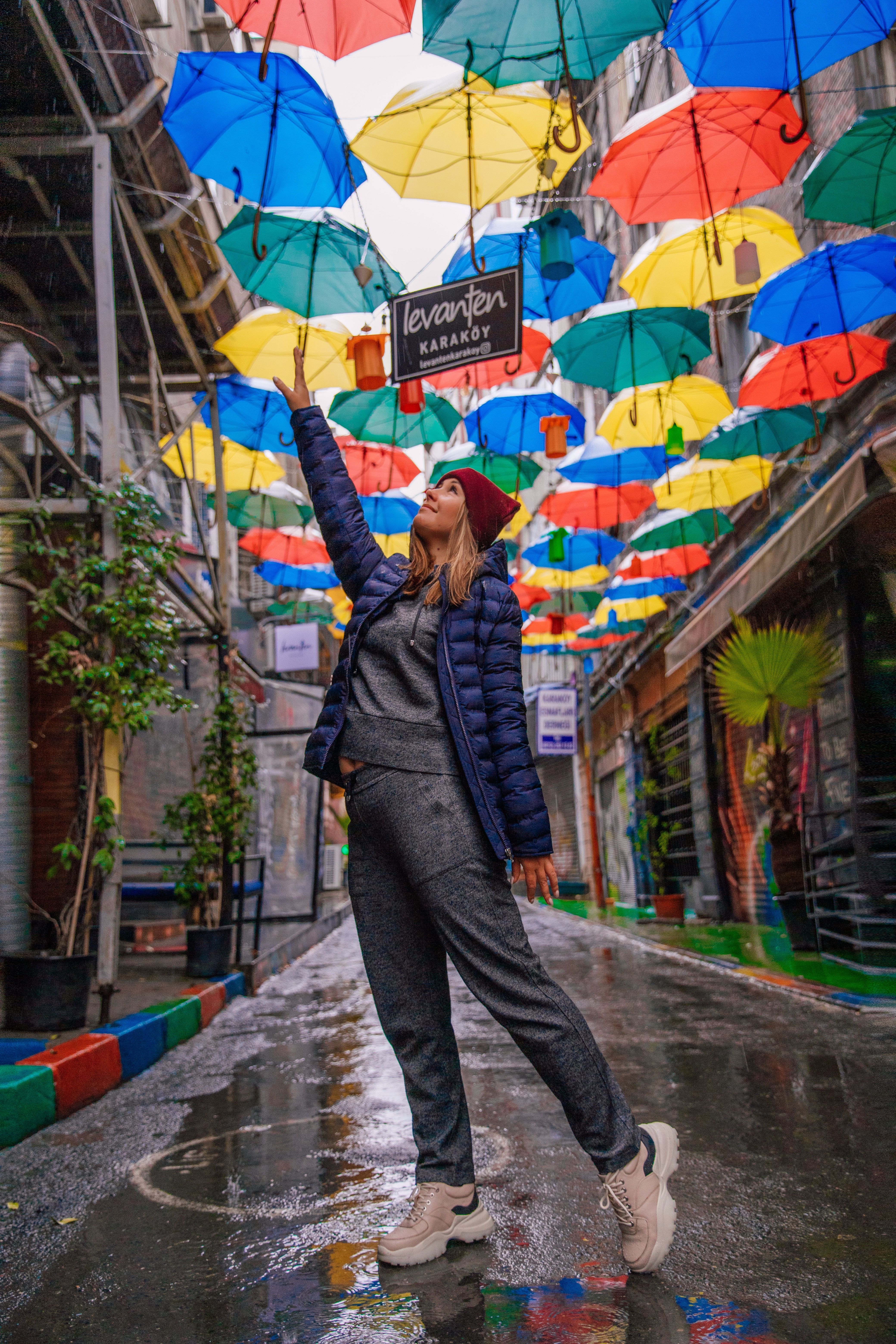 A woman reaches for vibrant umbrellas on a rainy Istanbul street.