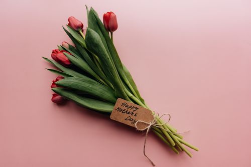Free Elegant bouquet of red tulips with 'Happy Mother's Day' tag on pink background, perfect for celebrating Motherhood. Stock Photo