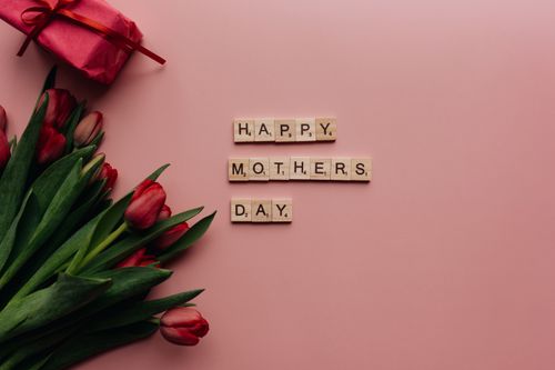 Free Mother's Day themed image featuring tulips and gift on a pink background with letter tiles spelling 'Happy Mother's Day'. Stock Photo