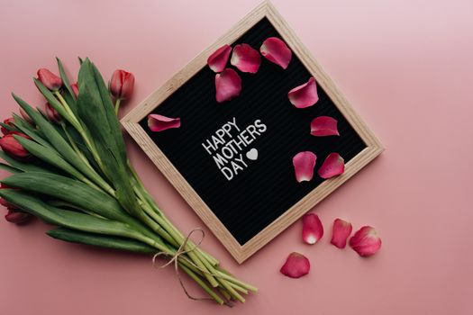Beautiful Mother's Day arrangement with tulips and letterboard on pink background.
