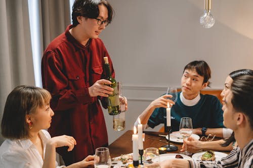 Group of People Looking at the Man Standing while Holding a Bottle of Wine