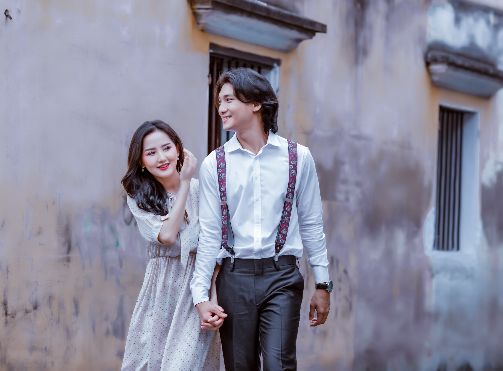 A young couple holding hands and walking together, dressed in stylish outfits, outdoors.