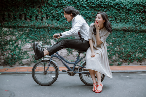 Free A joyful couple riding a bicycle together in a playful manner outdoors. Stock Photo