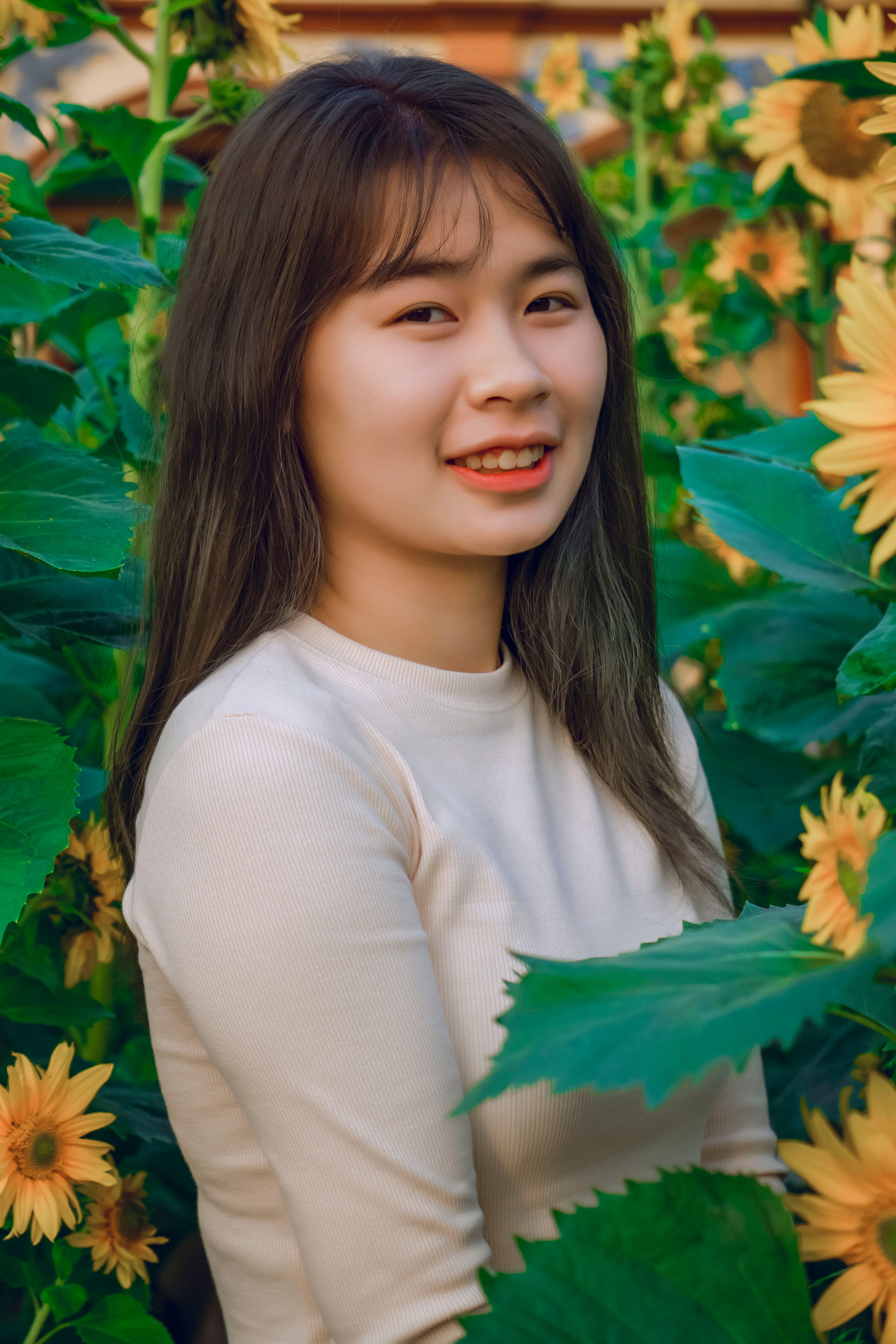 Charming young woman smiling while surrounded by lush sunflower blossoms, conveying warmth and joy.