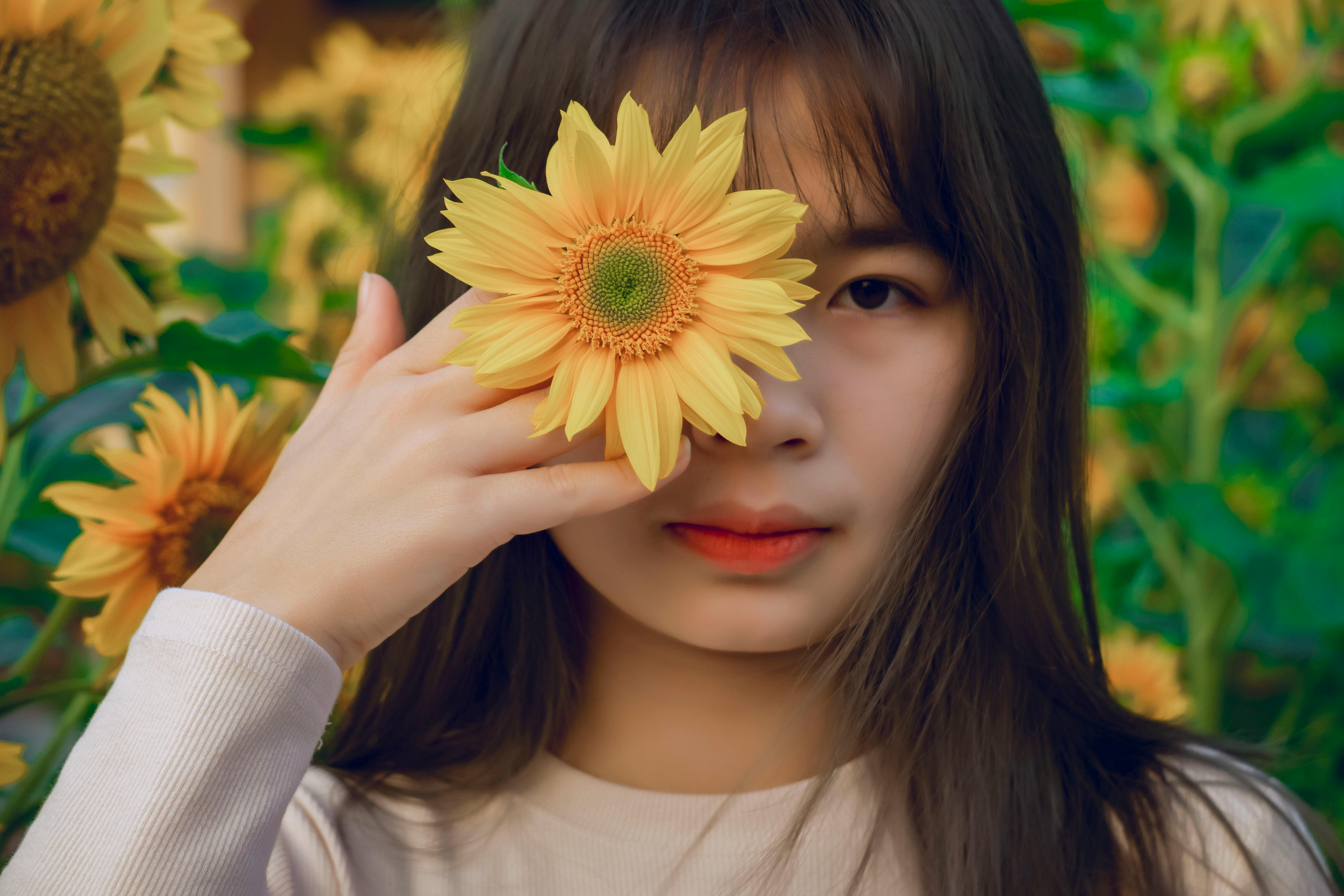 Close-Up Shot of a Pretty Woman Holding a Sunflower while Looking at Camera