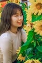 Close-Up Shot of a Pretty Woman in White Long Sleeves Looking at Blooming Sunflowers
