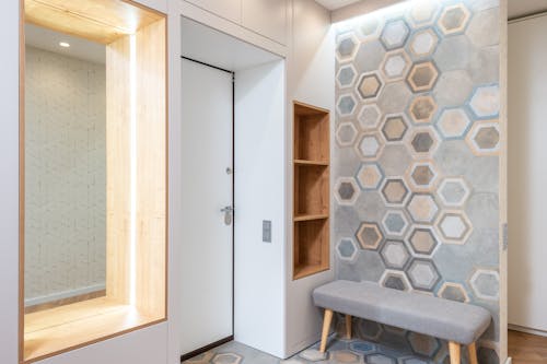 Lobby interior with entrance door and wall with hexagonal ornament against fabric bench and mirror with shiny light at home