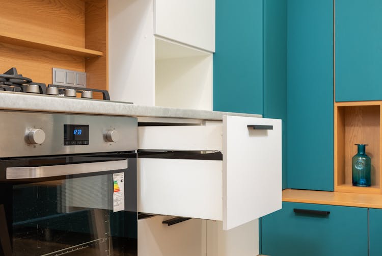 Open Drawer Of Cabinet Against Oven In Modern Kitchen