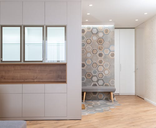 Free Glass cabinets in white kitchen against modern hallway with fabric bench and wall with hexagonal ornament Stock Photo