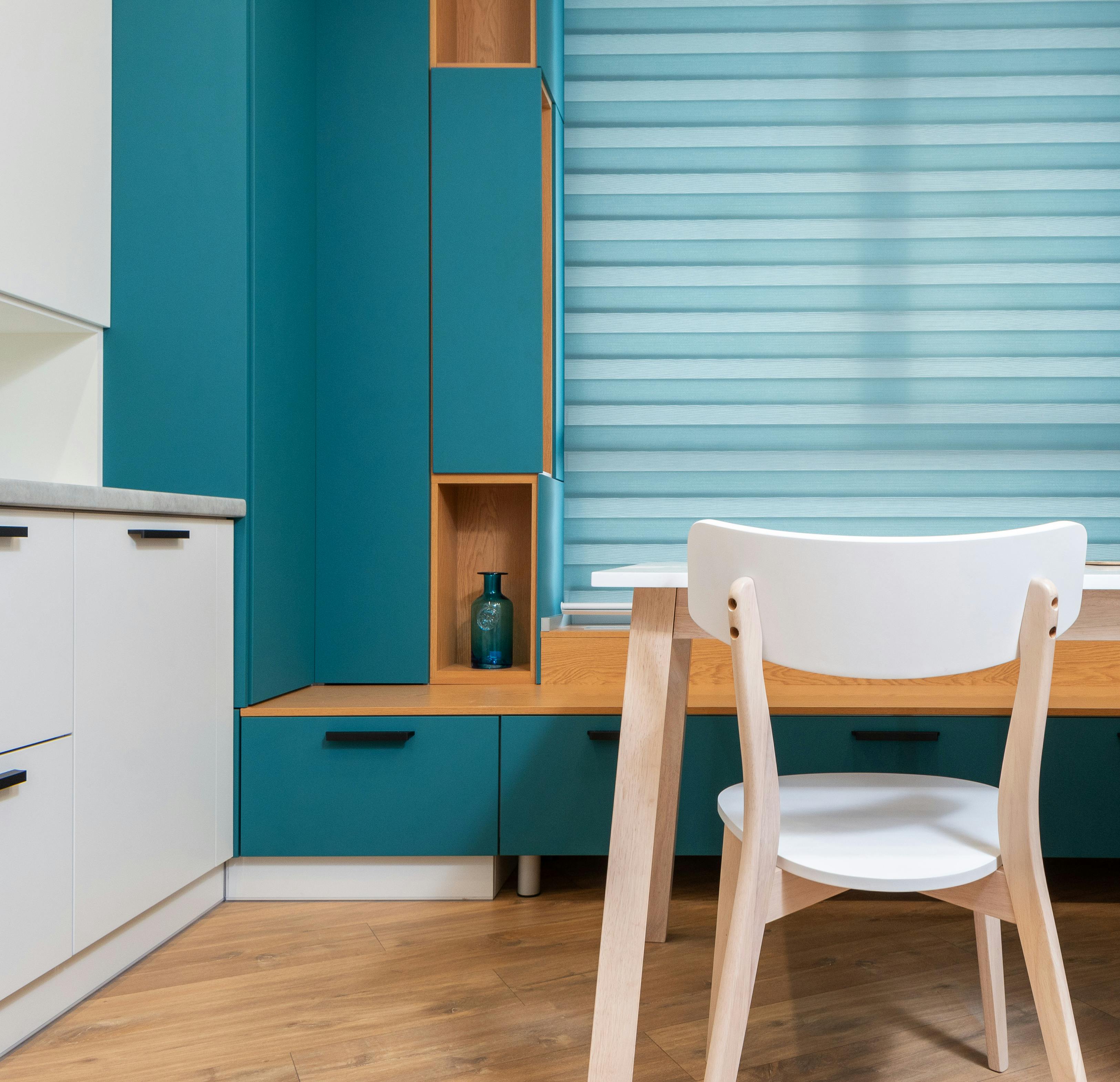 Modern kitchen interior with decorative vase on shelf of cabinet and window blind against table in house