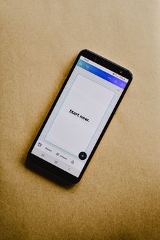 A smartphone displaying 'Start now' rests on a brown paper background, showcasing modern technology.