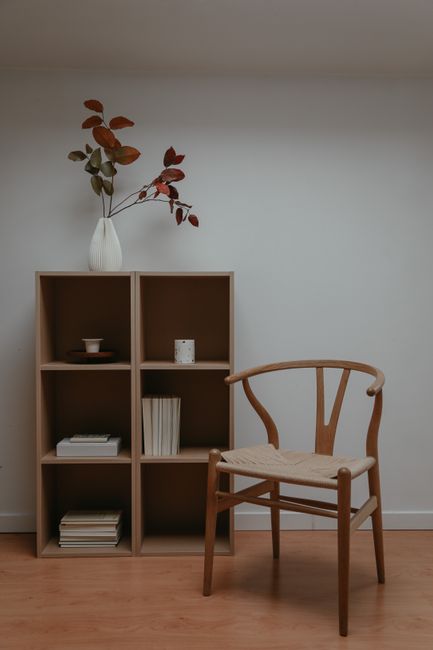 Stylish minimalist room featuring a wooden bookshelf and chair with decorative vase.