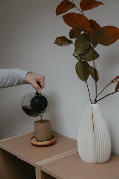 A minimalist setup featuring coffee being poured next to a decorative vase on a wooden cabinet.
