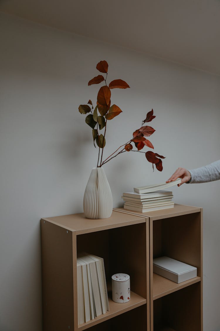 Photo Of A Person Getting A Book Near A White Vase