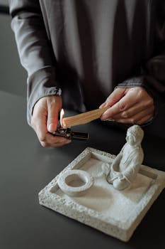 A person lights Palo Santo using a lighter near a zen statue, creating a calming atmosphere.