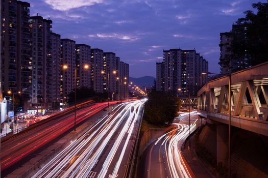 Dynamic view of Hong Kong's urban skyline with vibrant light trails on a busy highway at night.