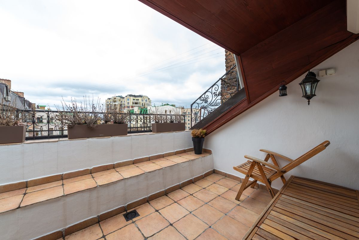Outdoor terrace with terracotta-coloured tiled flooring, raised tiled steps, planters, railing and seating.