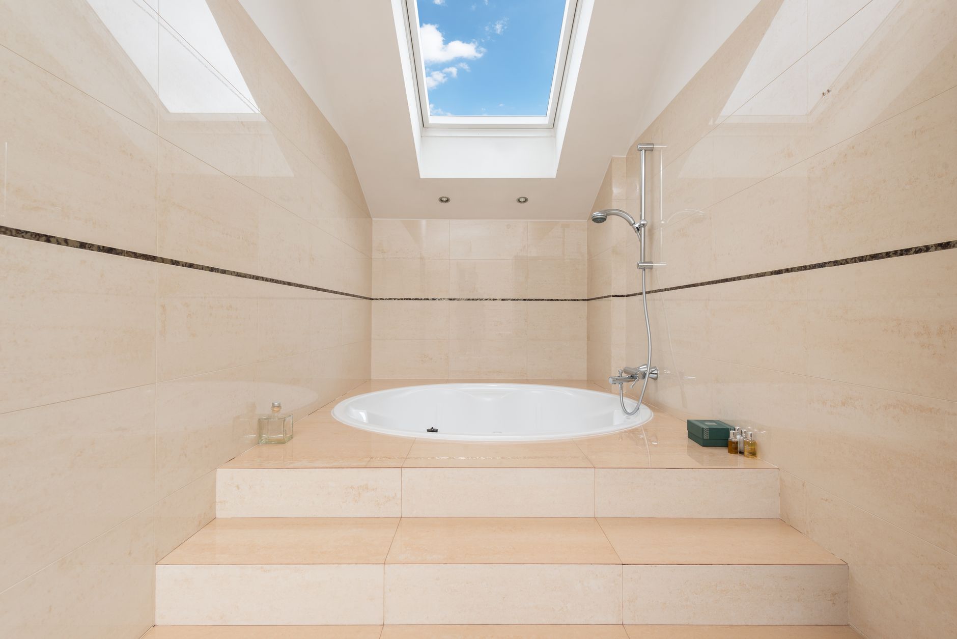 Contemporary bathroom interior with stairs and oval shaped bathtub under shower and cloudy blue sky in house